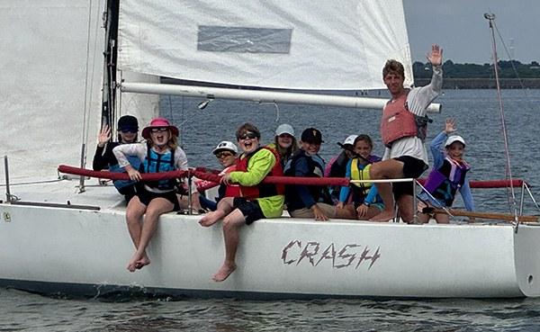 Youth sailors waving from the keelboat CRASH during sailing camp at Rush Creek